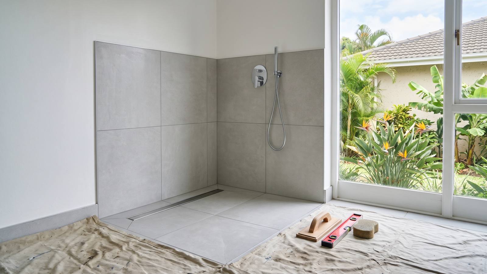 Freshly laid large-format light-grey porcelain tiles on a shower wall and floor with straight, even grout lines and a linear drain.